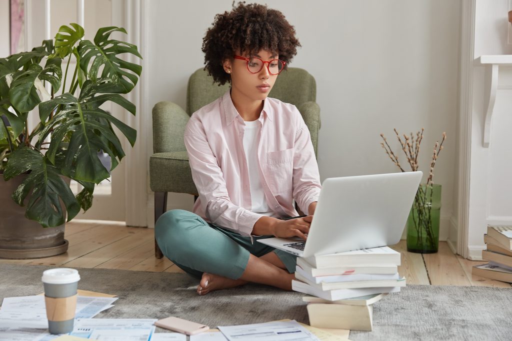 Women working ont he floor in her living room with her laptop stood on books